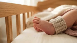 A newborn baby wearing a baby development tracking wearable on its tiny foot in a cozy nursery crib.